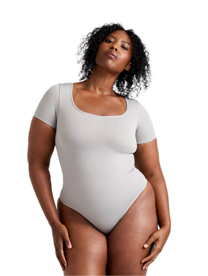 Woman wearing a light gray bodysuit against a white background